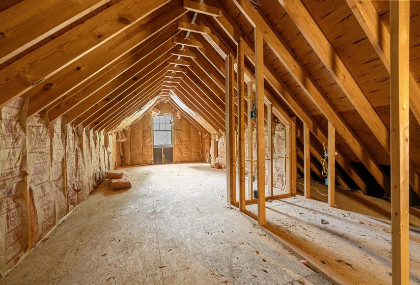 Unfinished attic space featuring exposed wood framing, ceiling rafters, insulation, a window, and wood subflooring