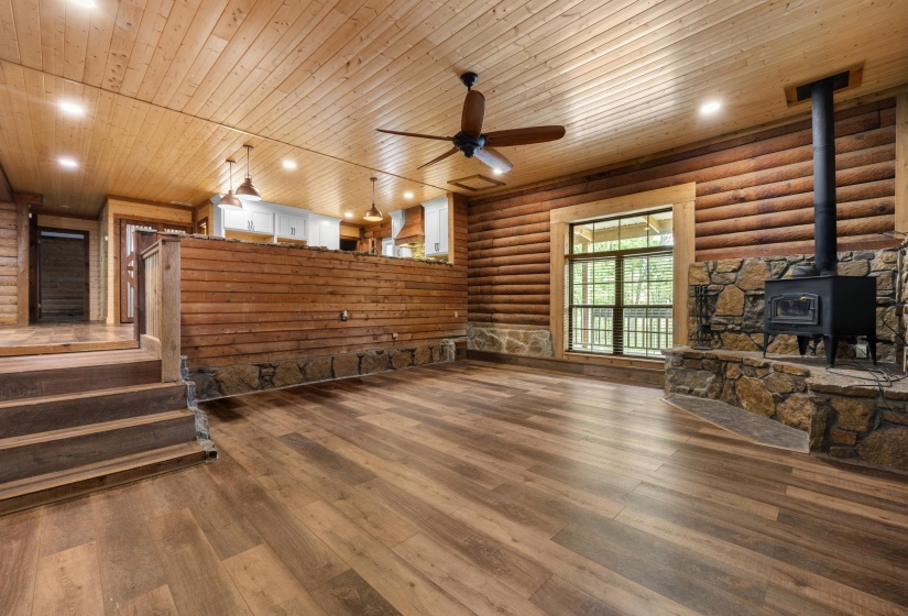 Spacious interior featuring wood-finish flooring, log walls, and a stone-clad wood-burning stove