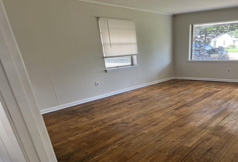 Spacious room featuring wood-finish flooring, light-toned wall paneling, white trim, and multiple windows