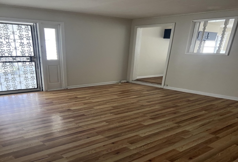 Spacious interior room featuring wood-finish flooring, light neutral walls, and white baseboards
