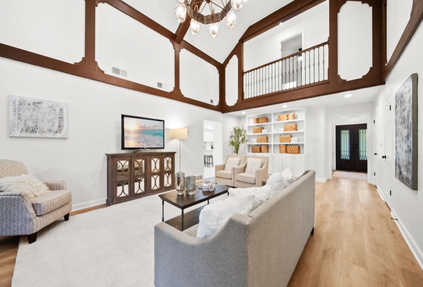 Vaulted ceiling with exposed wood beams, wood-finish flooring, built-in shelving, and a second-level balcony with metal balusters