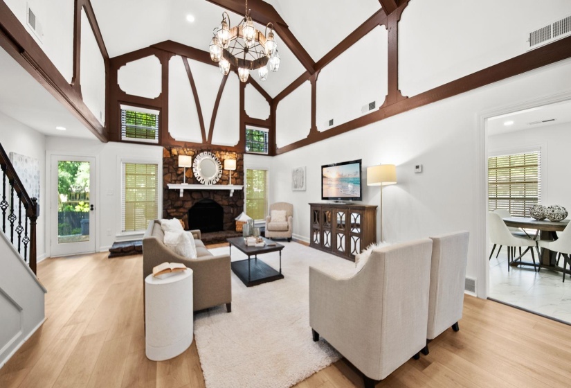 Spacious living area featuring a stone fireplace, vaulted ceilings with exposed beams, wood-finish flooring, and a glass-paneled exterior door