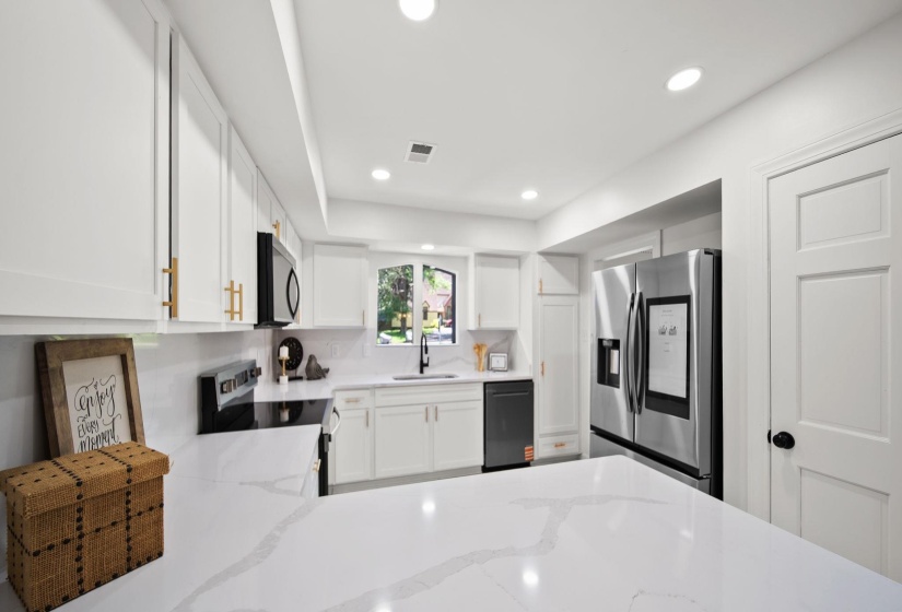 Bright kitchen featuring white cabinetry with gold-tone hardware, a quartz-finish countertop, and stainless steel appliances