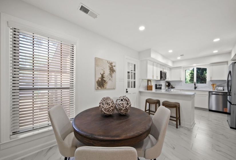 Open-concept living space featuring a kitchen with white cabinetry, stainless steel appliances, a white countertop island with seating, and recessed lighting