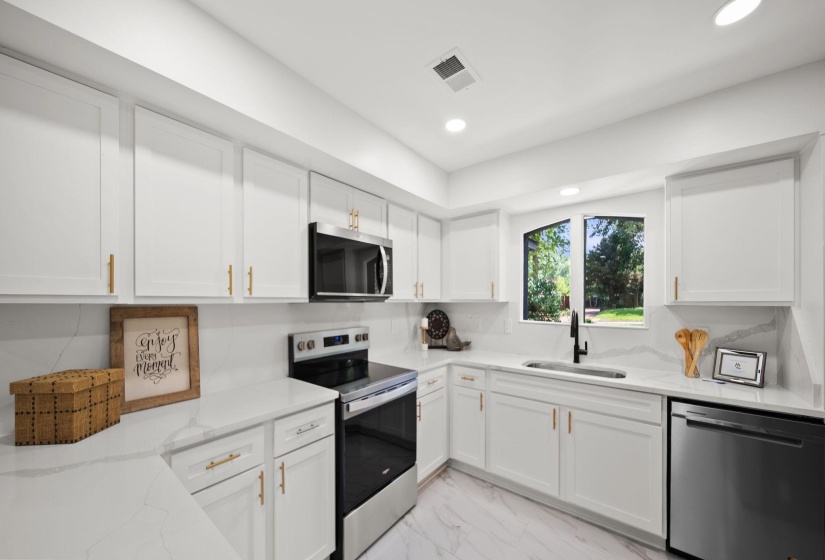 Modern kitchen featuring white cabinetry with gold-finish hardware, stainless steel appliances, white countertops, and recessed lighting