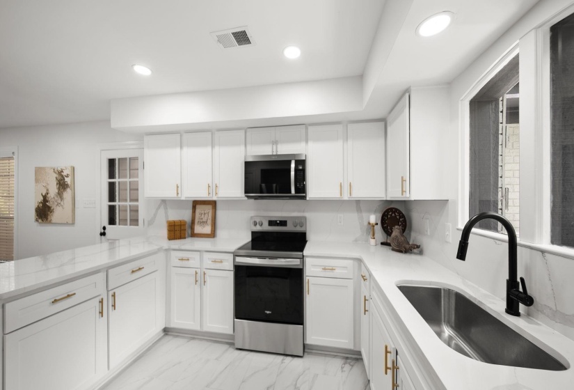 Contemporary kitchen featuring white cabinetry, quartz countertops with a matching backsplash, stainless steel appliances, and gold-tone hardware
