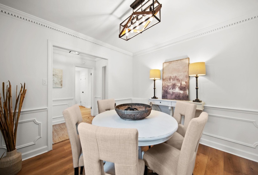 Dining area featuring wood-finish flooring, wainscoting, decorative crown molding, and an exposed linear chandelier