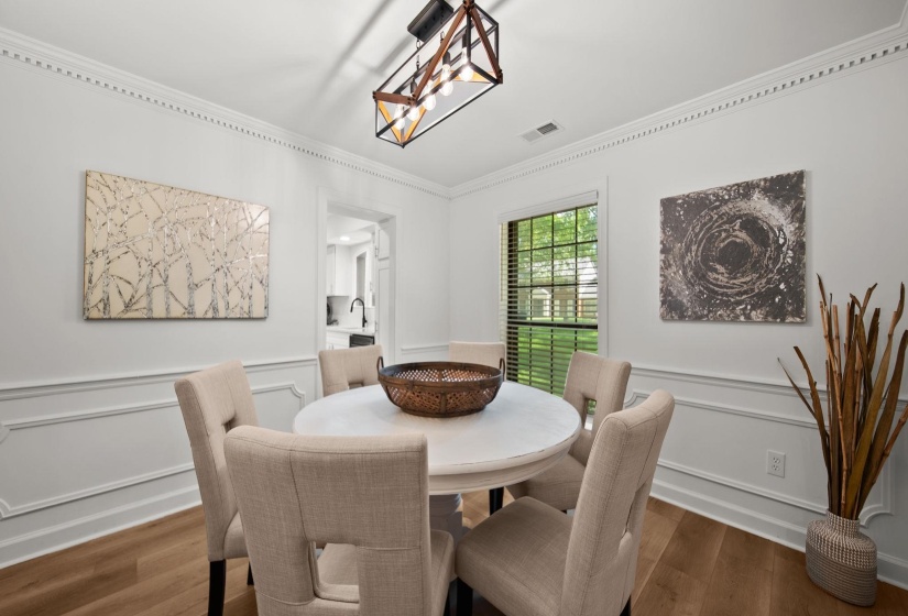 Dining space featuring crown molding, wainscoting, wood-finish flooring, a window with blinds, and an open archway to an additional room