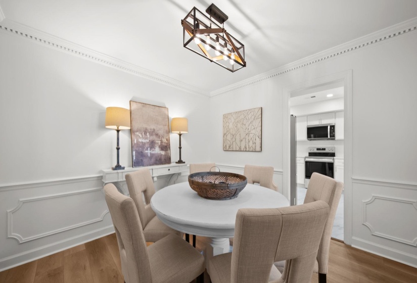 Dedicated dining area featuring wood-finish flooring, wainscoting, crown molding, and a contemporary ceiling fixture