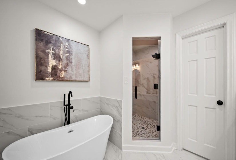 Freestanding soaking tub with matte black fixtures, marble-look tile, and a glass-enclosed shower featuring pebble flooring