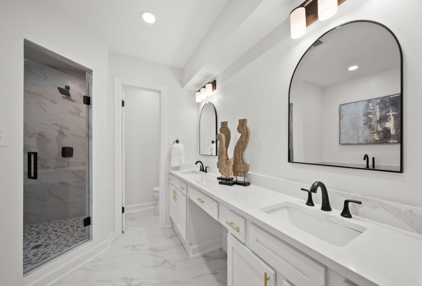 Spacious bathroom featuring a double vanity with white countertops, matte black fixtures, and arched mirrors
