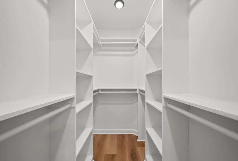 Walk-in closet featuring white built-in shelving, multiple hanging rods, recessed ceiling lighting, and wood-finish flooring