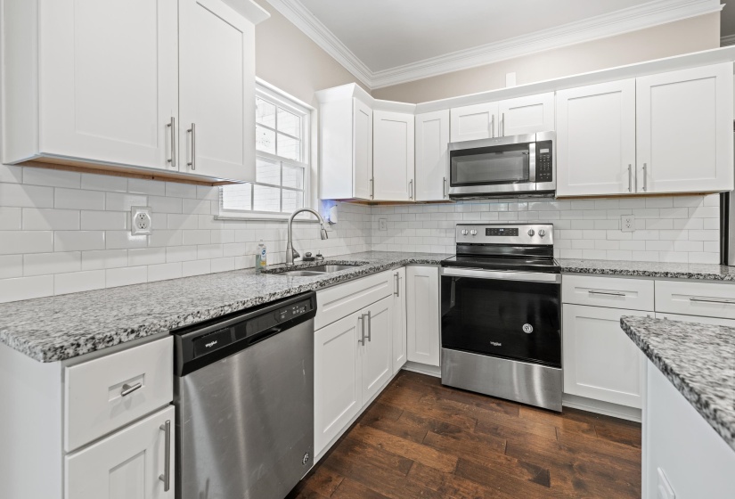 Kitchen featuring white cabinetry, stainless steel appliances, granite-style countertops, white subway tile backsplash, and wood-finish flooring