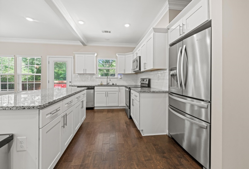 Contemporary kitchen with white shaker cabinetry, stainless steel appliances, speckled stone countertops, and wood-finish flooring