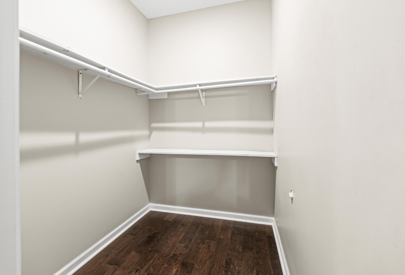 Walk-in closet featuring wood-finish flooring, white baseboards, light neutral wall paint, and white wire shelving with hanging rods
