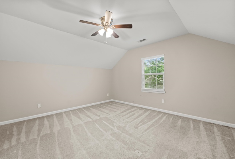 Spacious room featuring vaulted ceilings, a ceiling fan with integrated lighting, neutral wall tones, light-toned carpeting, and a window with blinds