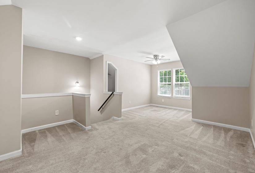 Spacious carpeted room featuring a ceiling fan, dual windows, and an angled ceiling line