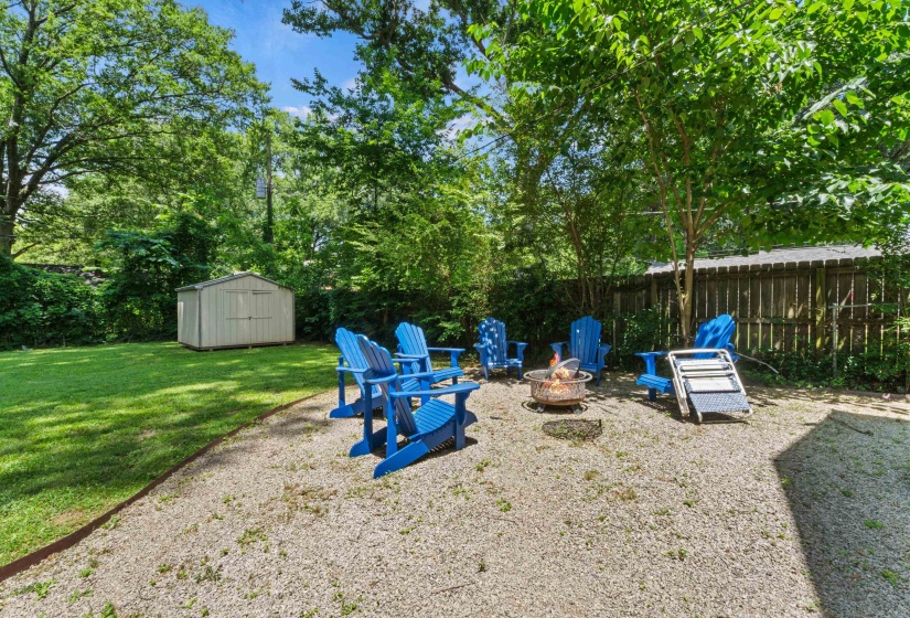 Expansive backyard featuring a gravel patio with a built-in fire pit, a manicured lawn, a detached storage shed, and a wood privacy fence