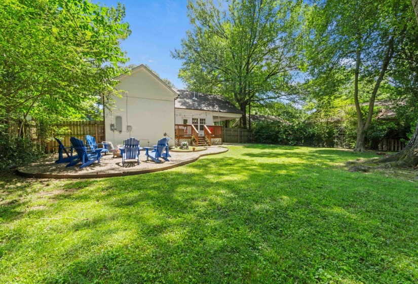 Spacious backyard featuring a large lawn area, mature trees, and a gravel patio with a curved wood border