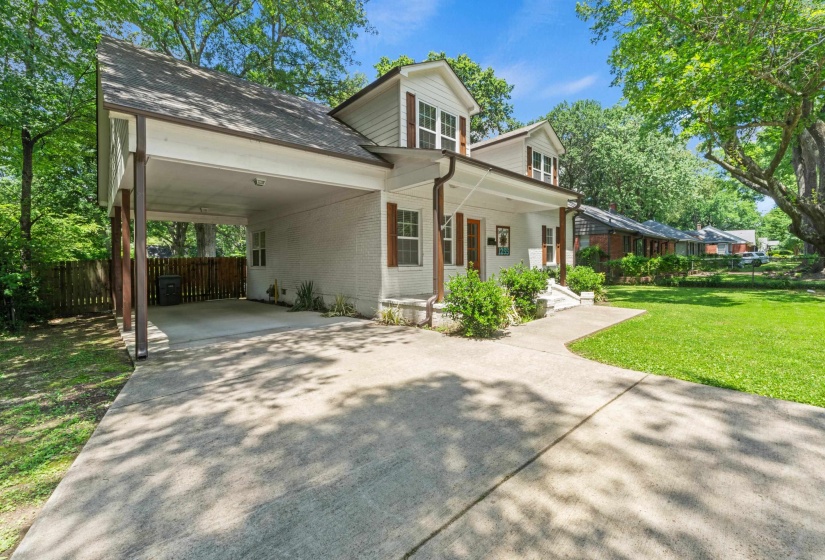 White exterior with brown accents, featuring a covered carport, concrete driveway, and front lawn