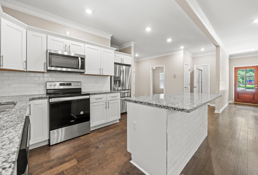 Kitchen featuring white cabinetry, stainless steel appliances, granite countertops, a white subway tile backsplash, and wood-finish flooring