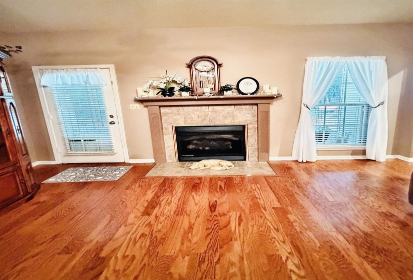 Living area featuring hardwood flooring, a tile-surround fireplace with a mantel, and a window with blinds