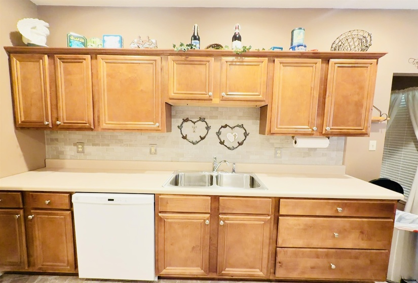 Kitchen featuring wood-finish cabinetry, a double basin stainless steel sink, beige countertops, and a tiled backsplash