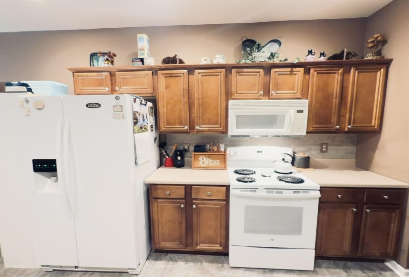 Kitchen with wood-finish cabinetry, white appliances, and light countertops