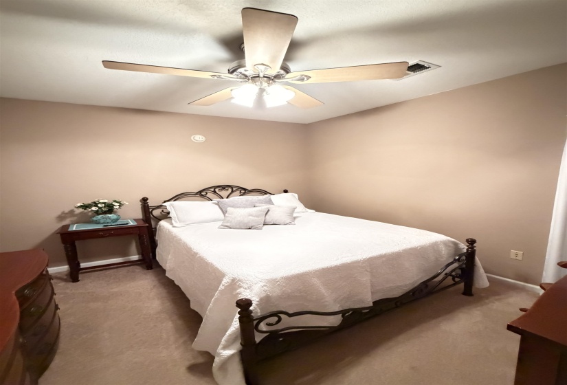 Carpeted bedroom featuring a ceiling fan with integrated lighting, neutral wall paint, and a wall-mounted electrical outlet
