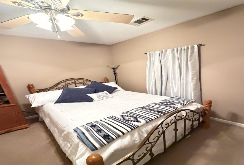 Neutral-toned room featuring a ceiling fan with light fixture and a window with light-filtering drapes