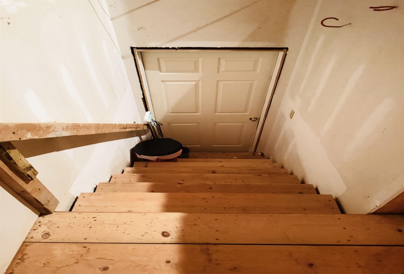 Unfinished wood staircase with white walls leading to a paneled door