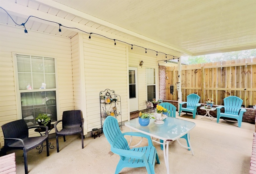 Covered patio with concrete flooring, accented by a new wood fence and brick detailing
