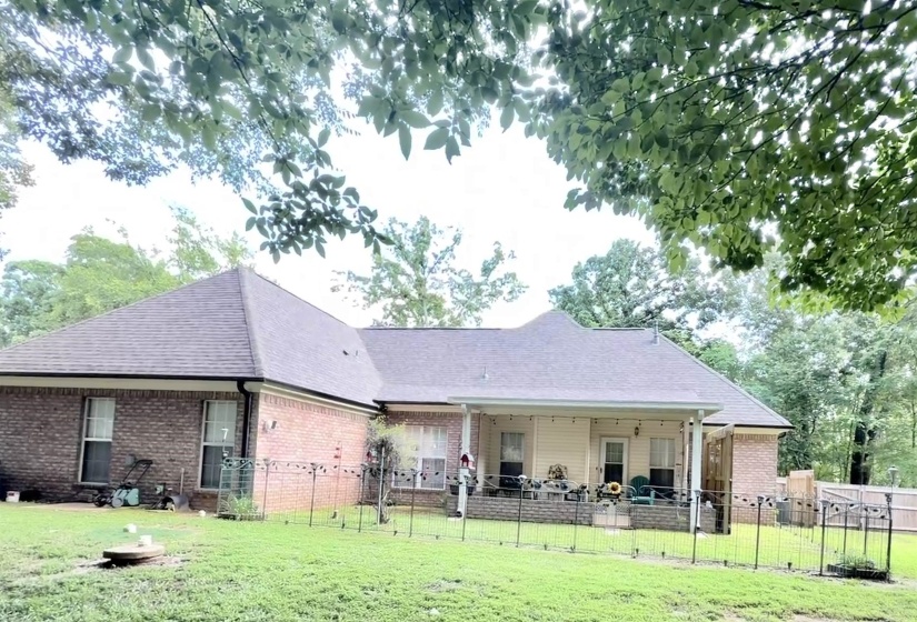 Brick exterior with a covered patio, fenced yard, and shingle roof