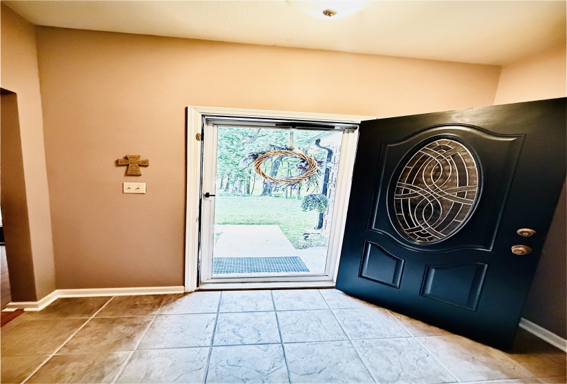 Entryway featuring textured tile flooring, a decorative front door with an oval glass insert, and a storm door