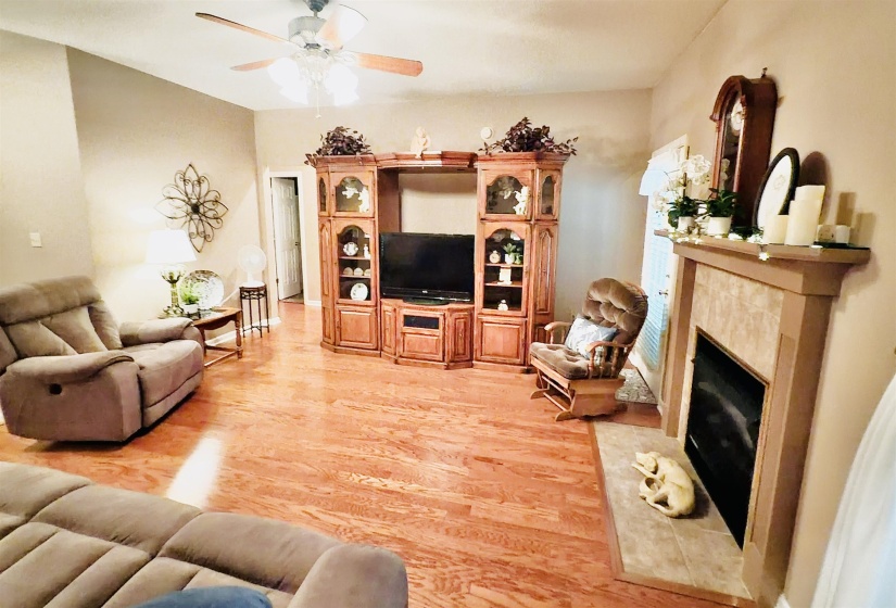 Spacious living area featuring wood-finish flooring, a ceiling fan with light fixture, and a built-in media center with display shelving