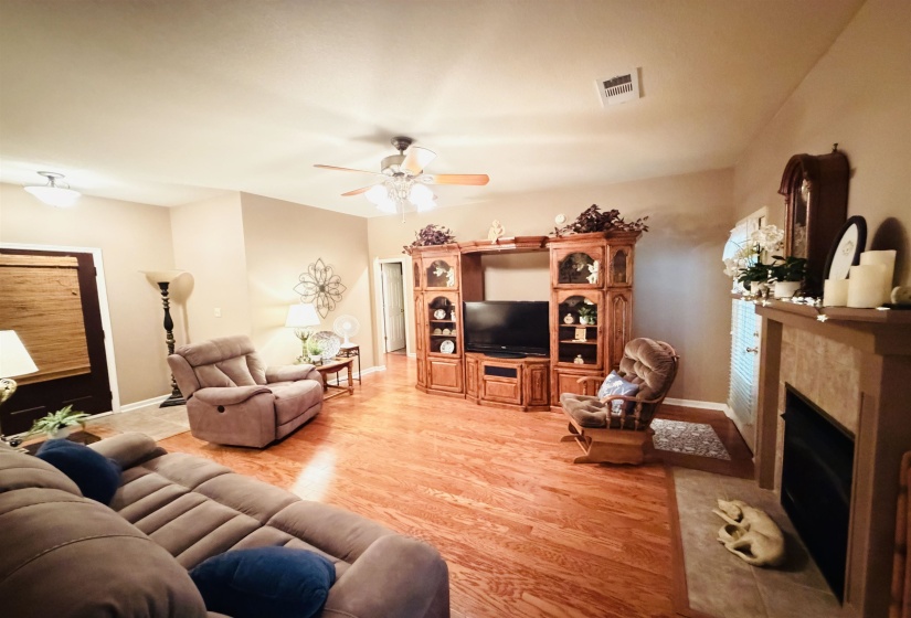 Spacious living area featuring wood-finish flooring, a ceiling fan with integrated lighting, and neutral-toned walls