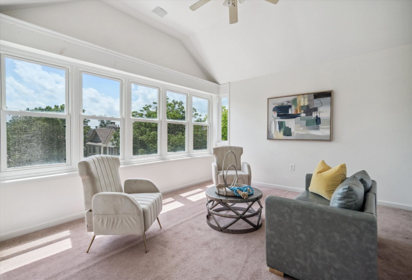 Bright room featuring a vaulted ceiling with a ceiling fan, a wall of multiple windows, and light-colored carpeting