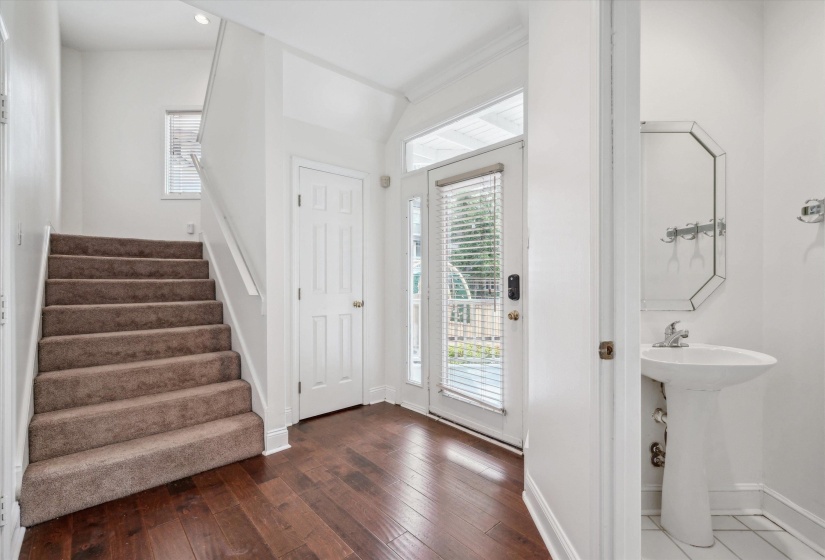 Entryway featuring dark wood-finish flooring, a carpeted staircase with a white handrail, and a white six-panel door