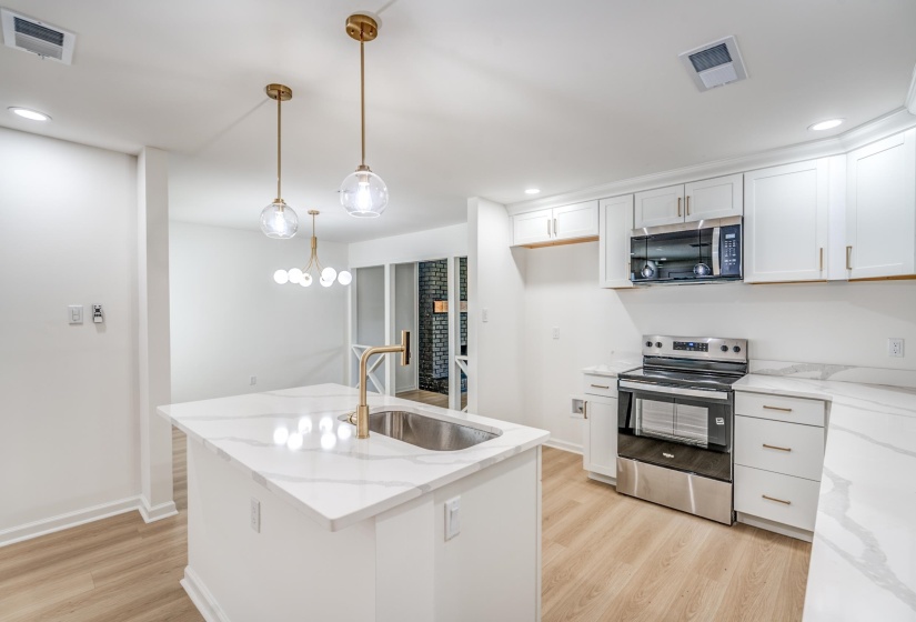 Kitchen featuring a central island with an undermount sink and gold-tone faucet, white cabinetry with gold-tone hardware, stainless steel appliances, and wood-finish flooring