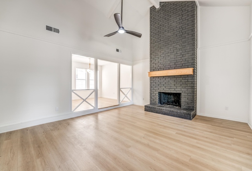 Spacious room featuring a floor-to-ceiling brick fireplace with a wood mantle, vaulted ceilings, and wood-finish flooring