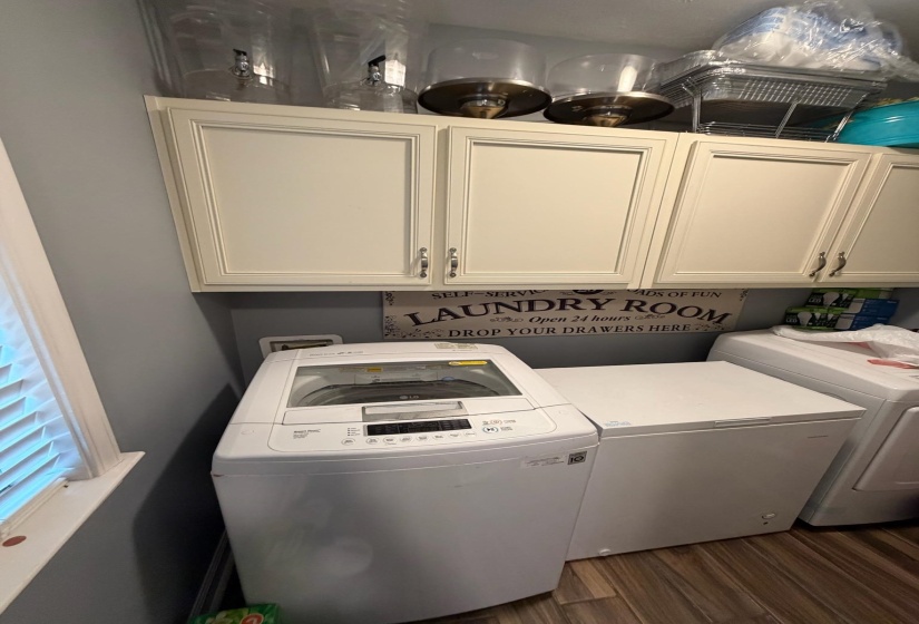 Laundry area featuring upper cabinetry with brushed nickel hardware, light blue wall paint, and wood-finish flooring