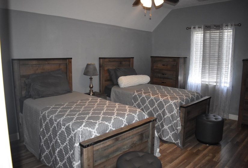 Vaulted ceiling room with wood-finish flooring, neutral gray walls, and a window with blinds