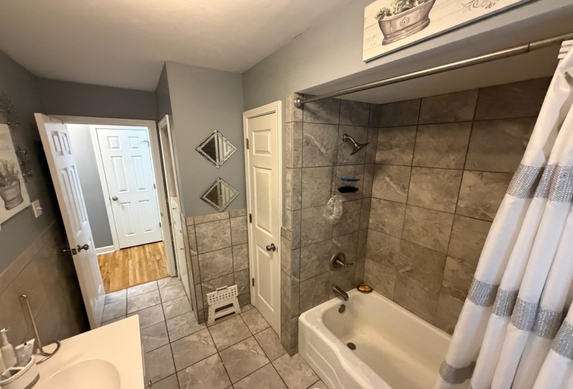 Bathroom featuring a built-in tub with shower, gray tiled walls, and a white vanity with an integrated sink
