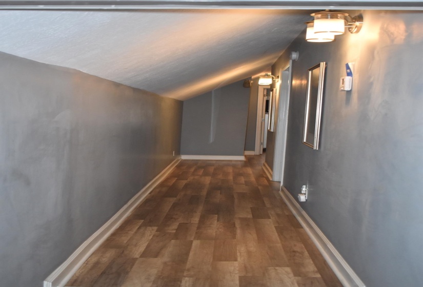 Hallway featuring wood-finish flooring, grey wall paint, and white baseboards