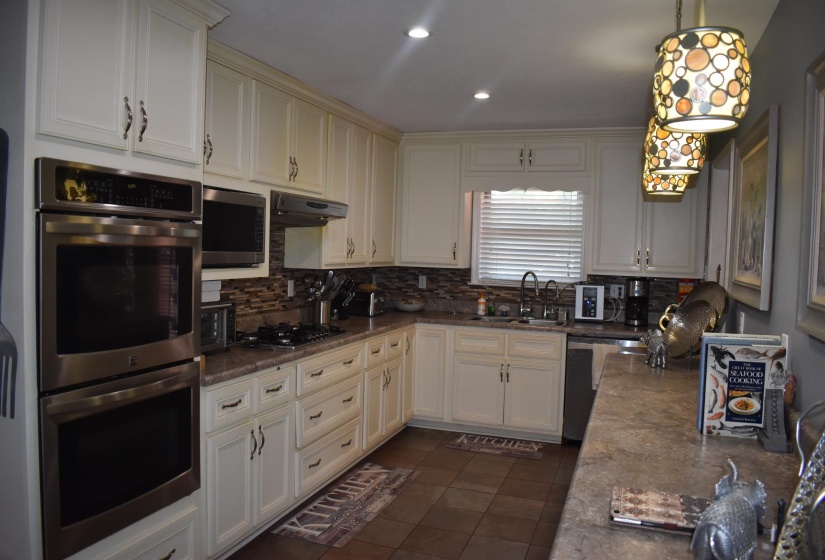 Kitchen featuring white cabinetry, stainless steel double wall ovens, a gas cooktop, mosaic tile backsplash, and a double basin sink
