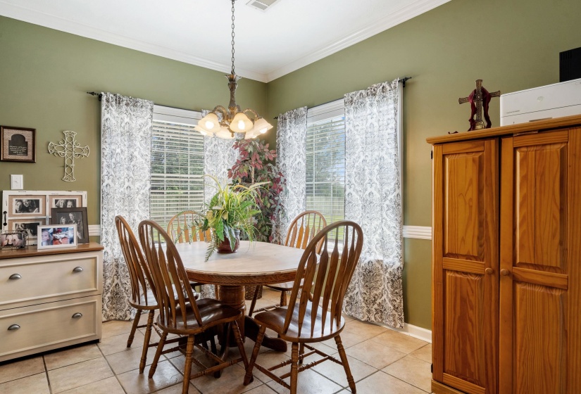 Dining area featuring tile flooring, a window with blinds and patterned curtains, a chandelier, and crown molding