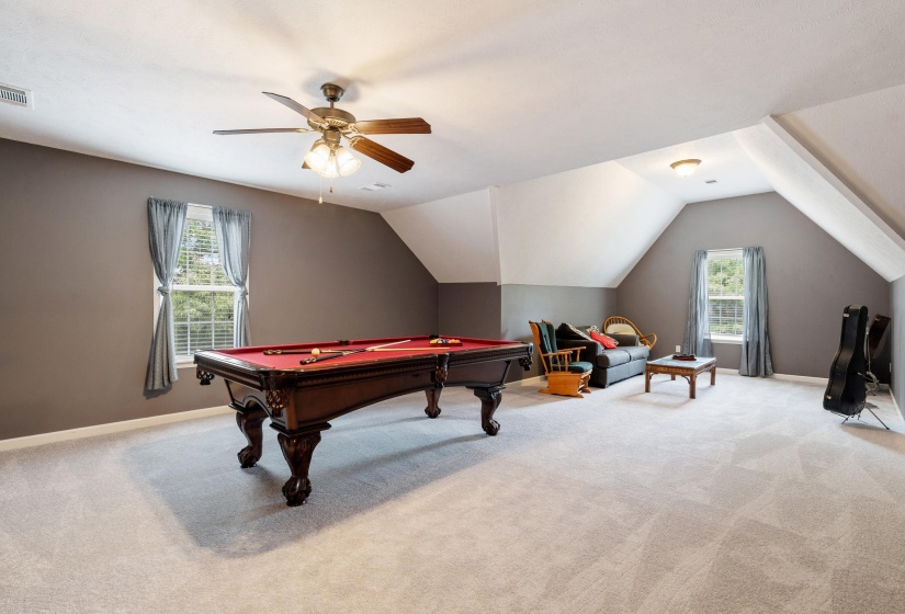 Spacious bonus room featuring light-colored carpeting, multiple windows, and a ceiling fan with integrated lighting