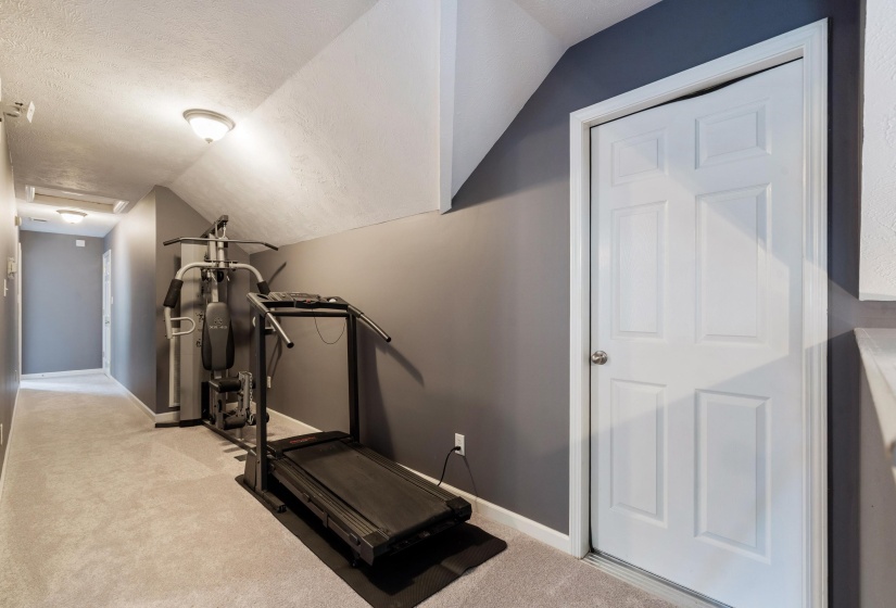 Carpeted hallway featuring a paneled interior door, sloped ceilings, recessed lighting, and neutral wall tones