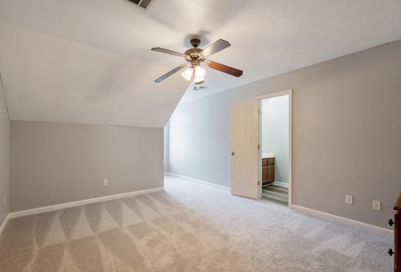 Carpeted room with a ceiling fan, sloped ceiling detail, and a doorway revealing a vanity with wood-finish cabinetry