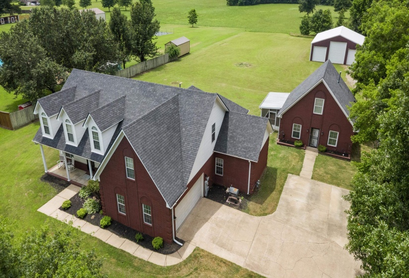 Expansive property featuring a brick main residence with a front porch and dormer windows, an attached garage, and a separate brick structure